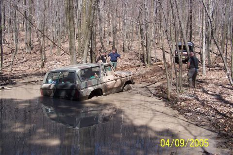 1979 Ford Bronco - A camouflaged 1979 Ford Bronco is stuck in a mud pit while another vehicle waits in the background.