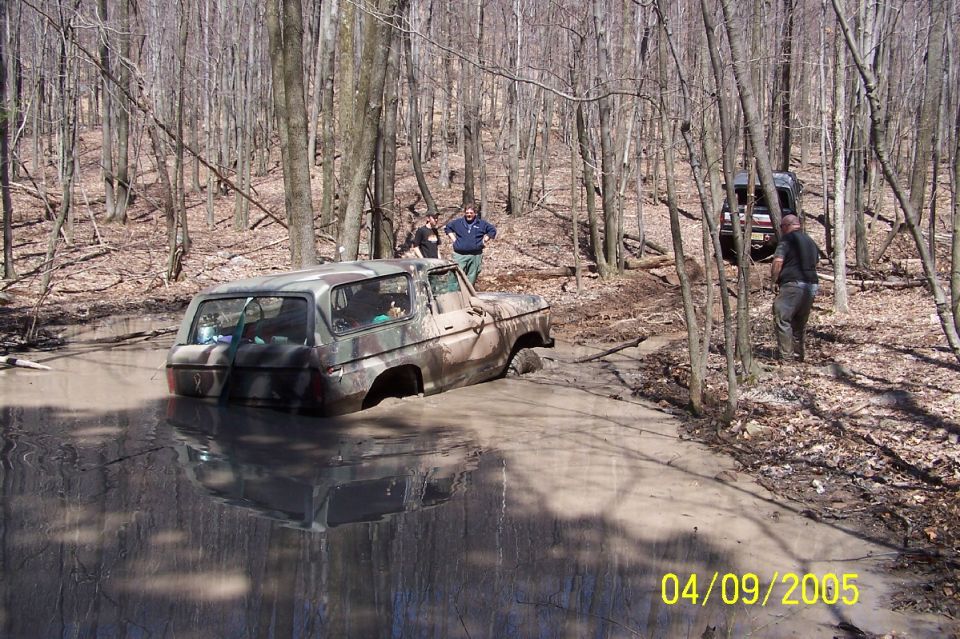 Camouflaged 1979 Ford Bronco stuck in mud pit, rear view