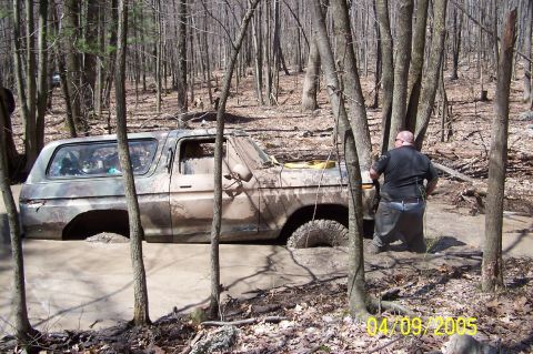 1979 Ford Bronco - A person stands near a muddy 1978 Ford Bronco stuck in a ditch in a wooded area.
