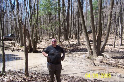 1979 Ford Bronco - A man stands in a muddy forest clearing, with two off-road vehicles visible in the background.