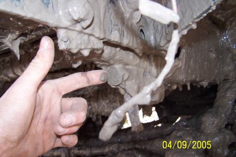 1979 Ford Bronco - Close-up of a muddy vehicle's undercarriage with a hand pointing at a bolt.