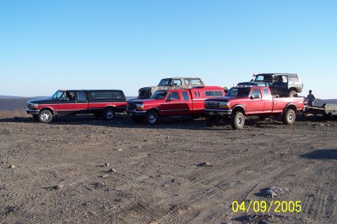 1979 Ford Bronco - A group of trucks and an SUV are parked together on a dusty, open area.