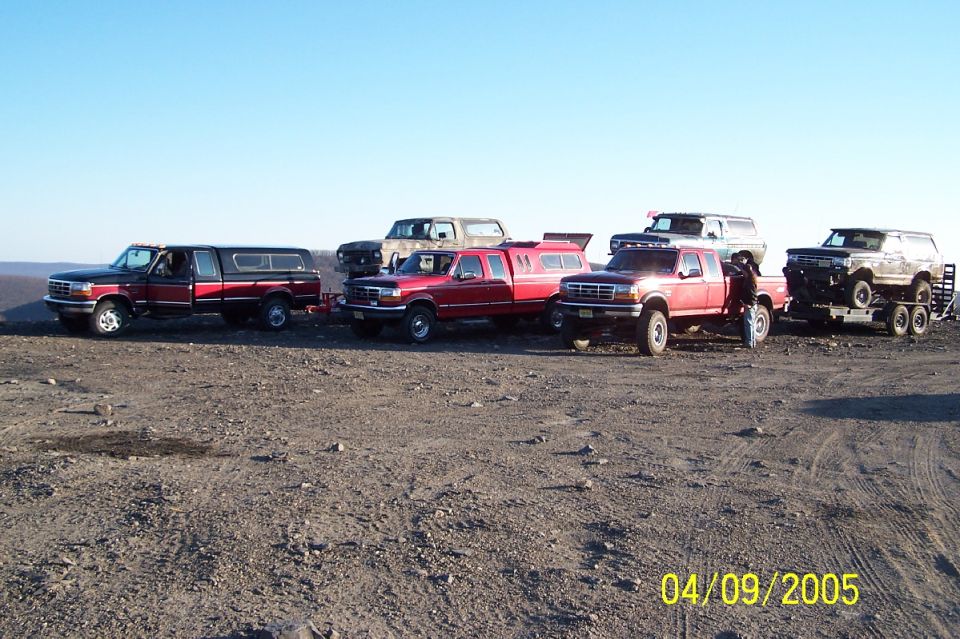 Several Ford trucks and SUVs parked on a dirt lot under a clear blue sky