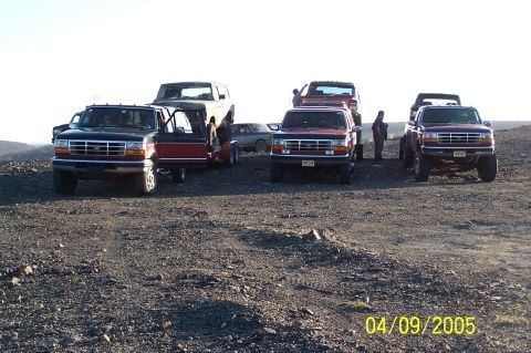 1979 Ford Bronco - A group of Ford trucks and SUVs are gathered on a rocky landscape, with one truck carrying another vehicle on a trailer.