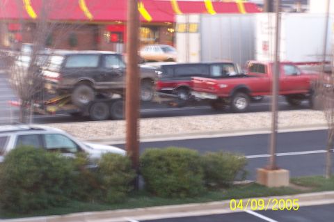 1979 Ford Bronco - A black Ford Bronco is transported on a trailer, accompanied by other vehicles on the road.