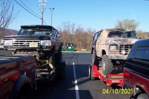 1979 Ford Bronco - Two lifted Ford trucks are parked side-by-side on trailers under a clear sky.