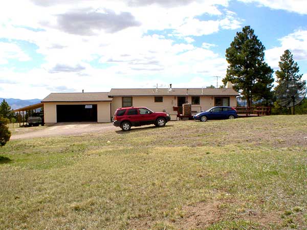 Dark red SUV parked by a tan house with garage, blue wagon nearby, rural landscape.