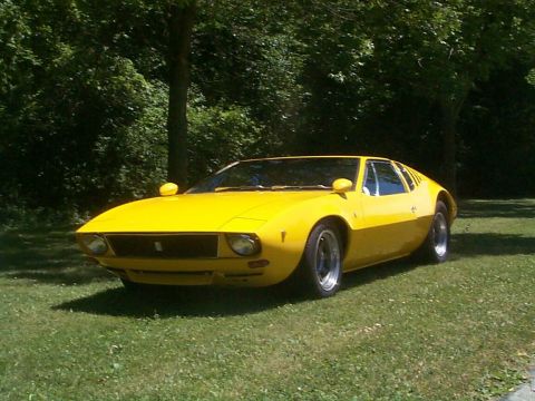 1968 Ford Mustang - A bright yellow sports car is parked on a grassy lawn with trees providing shade.