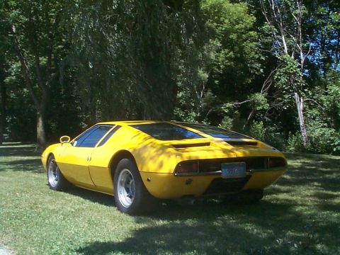 1968 Ford Mustang - A yellow sports car is parked on a grassy area with trees in the background.