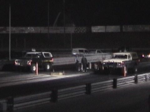 1978 Ford Bronco - Two SUVs are lined up on a drag strip at night, with spectators visible in the background.