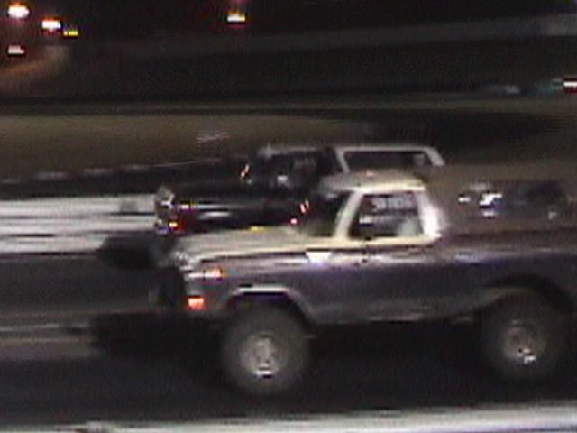 1978 Ford Bronco driving on a track at night, another vehicle behind it