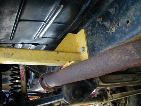1979 Ford Bronco - The underside of a vehicle reveals a rusty exhaust system and a yellow support structure, with a Rancho shock absorber in view.