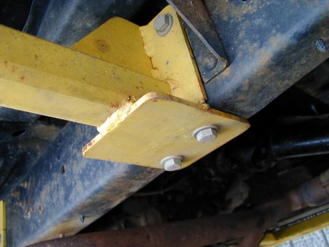 1979 Ford Bronco - Close-up view of a yellow metal bracket attached to the vehicle's frame, with visible bolts and rust.
