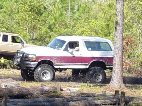 1989 Ford Bronco - A lifted Ford Bronco navigates a muddy terrain with another vehicle visible in the background.