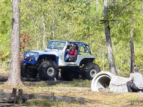 1989 Ford Bronco - A modified off-road jeep with oversized tires navigates a wooded area, with a person observing nearby.