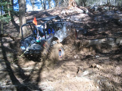 1995 Ford Bronco - An off-road vehicle navigates a muddy incline in a wooded area.