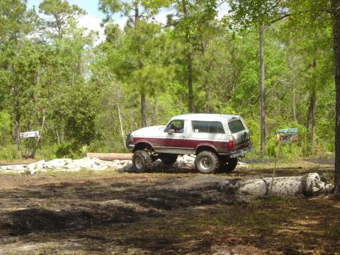 1993 Ford Bronco - Ford Bronco navigating a muddy off-road trail with trees in the background.