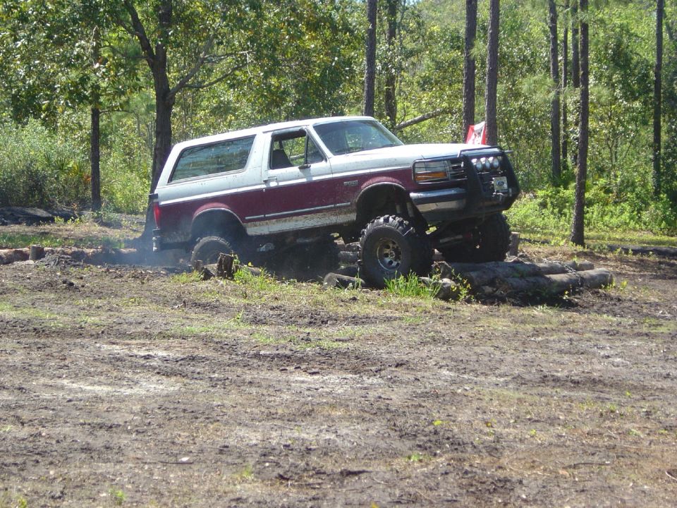 Maroon and white 1993 Ford Bronco off-roading over logs