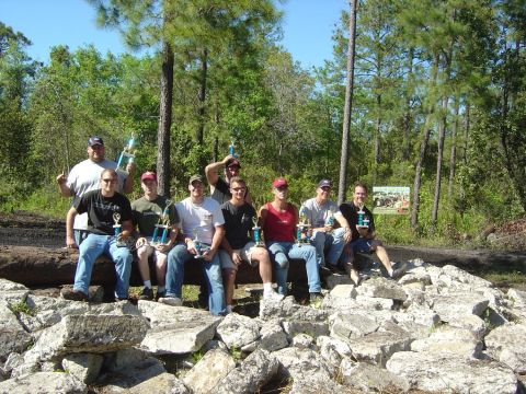 1993 Ford Bronco - Men pose with trophies after an event, seated on a log and rocks in a wooded area.