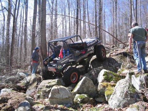 1995 Ford Bronco - A modified off-road vehicle navigates a challenging rocky terrain in a forest setting.