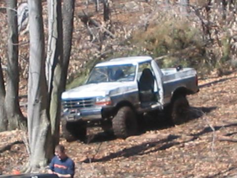 1995 Ford Bronco - This lifted Ford truck is parked off-road with its doors open, surrounded by trees and fallen leaves.