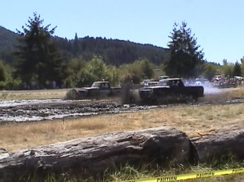 1978 Ford Bronco - Trucks navigate a muddy track during an event, kicking up spray.