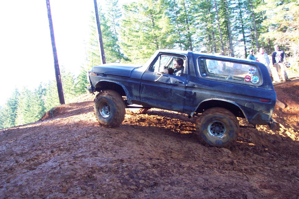 Dark blue 1978 Ford Bronco climbing a muddy hill with trees in the background