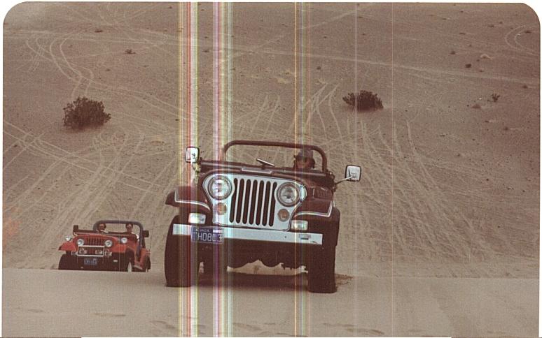 Two Jeeps driving on sand dunes, one in front and one smaller one behind