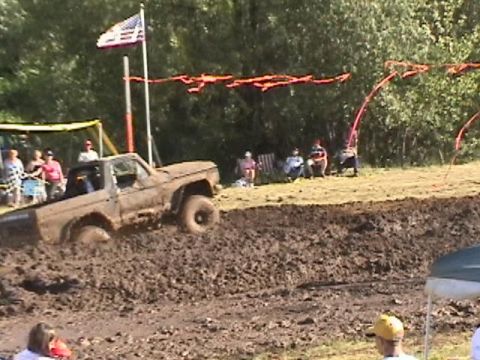 1978 Ford Bronco - A truck navigates a challenging mud bog during an event with an American flag flying.