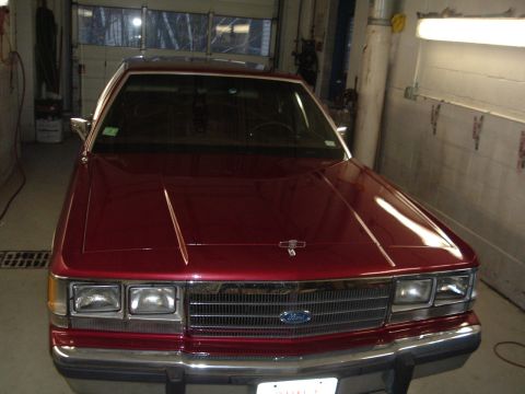 2001 Ford Crown Victoria - Front view of a red sedan with a chrome grille and headlights, parked in a garage.