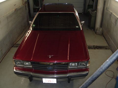 2001 Ford Crown Victoria - This red sedan features a prominent chrome grille and rectangular headlights, suggesting an older model year.