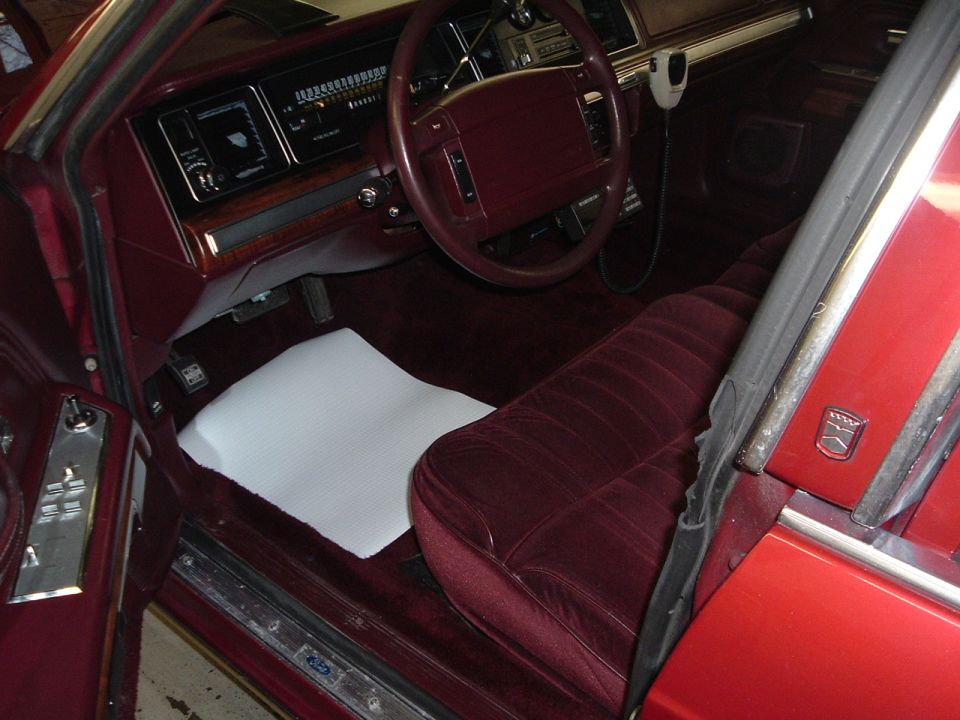 Interior view of a red car with maroon velour seats and dashboard. A white mat covers the floor