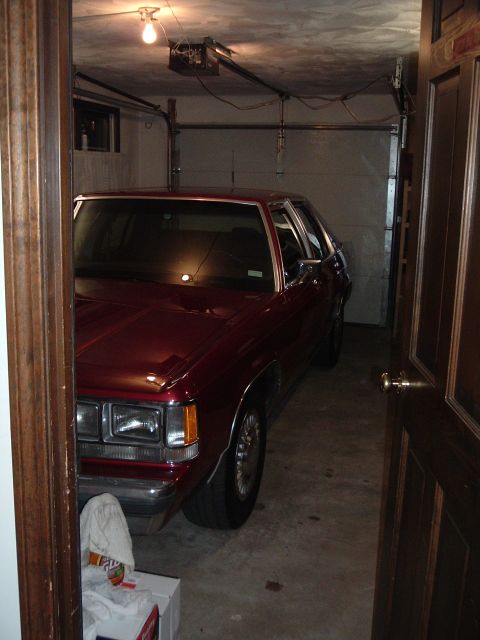 2001 Ford Crown Victoria - A maroon sedan is parked inside a garage, partially obscured by a doorway.