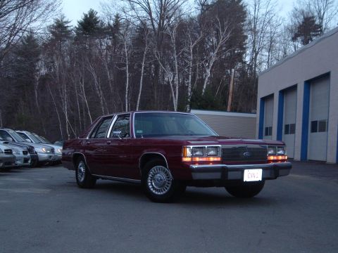 2001 Ford Crown Victoria - A maroon 2001 Ford Crown Victoria sedan is parked in front of a building with garage doors.