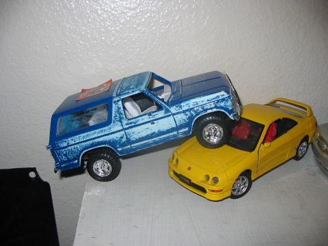 1986 Ford Bronco - Toy Bronco model is precariously balanced on top of a yellow Acura model.