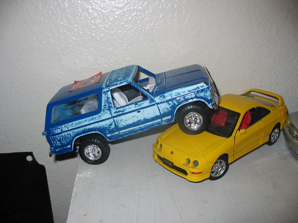 Toy blue Bronco model on top of a yellow toy Acura model