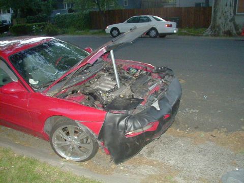 1993 Ford Probe - A red 1993 Ford Probe sits on the side of the road with its hood up, revealing the engine and a damaged front end.