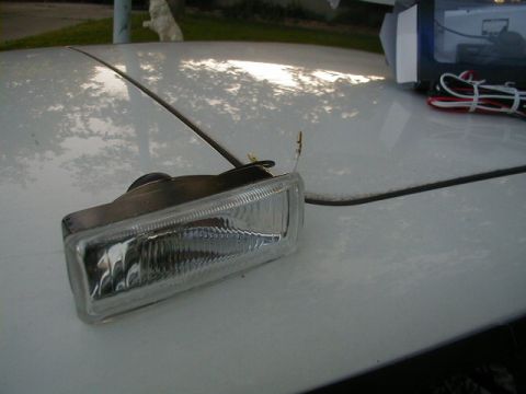 1993 Ford Probe - A clear fog light with wiring is placed on the hood of a white vehicle, with a box of parts in the background.