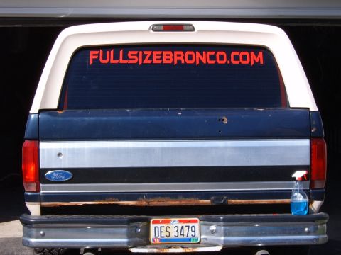1993 Ford Bronco - Rear view of a dark blue and white full-size Ford Bronco with a red FULLSIZEBRONCO.COM windshield banner across the rear glass. The tailgat…