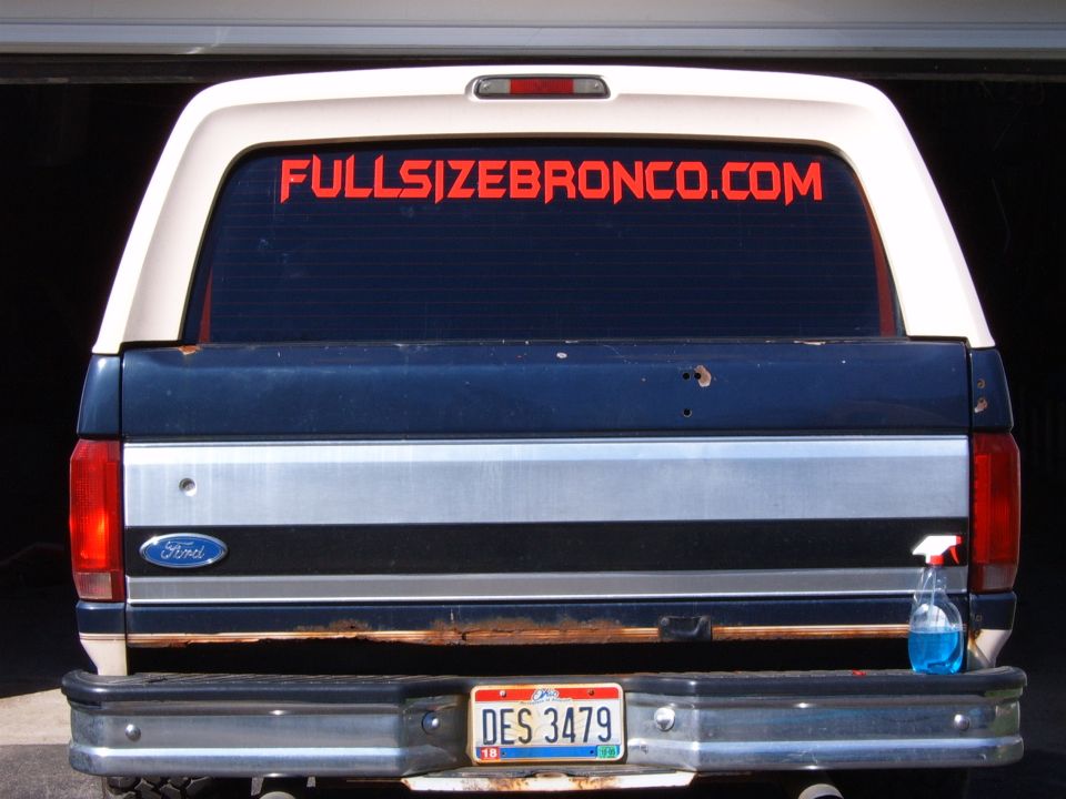 Rear of blue and white Ford Bronco with FULLSIZEBRONCO.COM rear window decal and rusty tailgate