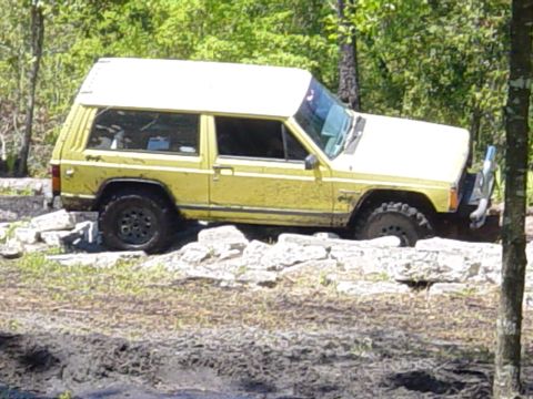 1989 Ford Bronco - A yellow Jeep Cherokee with a white roof navigates a rocky terrain.