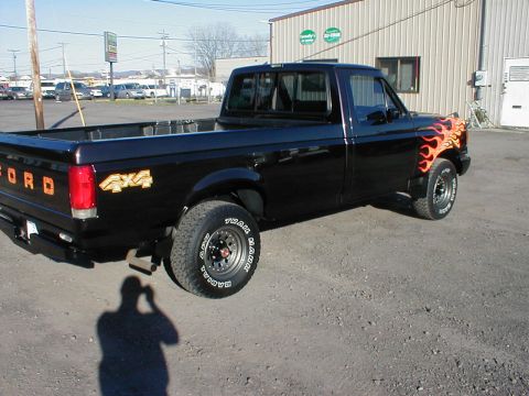 1991 Ford F-150 - A black pickup truck is parked outside a building. It has flame decals on the front fender and '4x4' graphics on the bed.