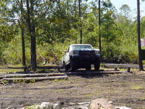 1989 Ford Bronco - A white pickup truck navigates an obstacle course made of logs in a forest setting.
