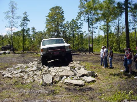 1989 Ford Bronco - A white SUV navigates a rocky obstacle course, with spectators watching the event.