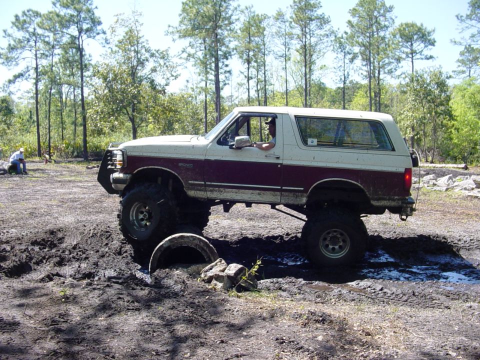 Two-tone lifted 1989 Ford Bronco navigating a muddy off-road course