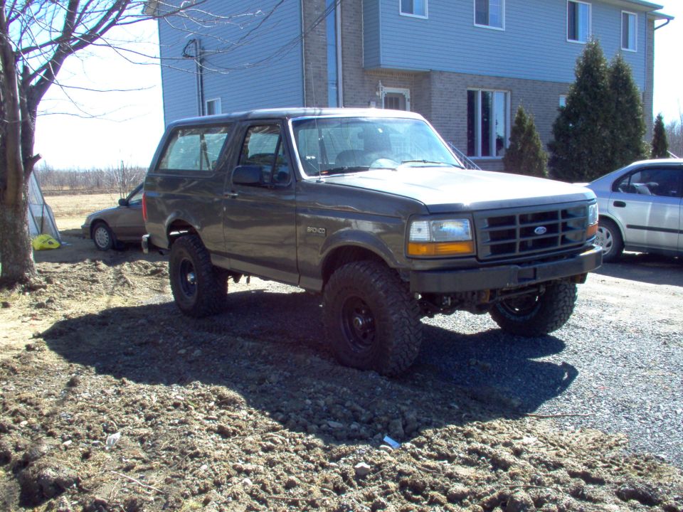 Gray 1993 Ford Bronco parked on dirt with a silver sedan in the background