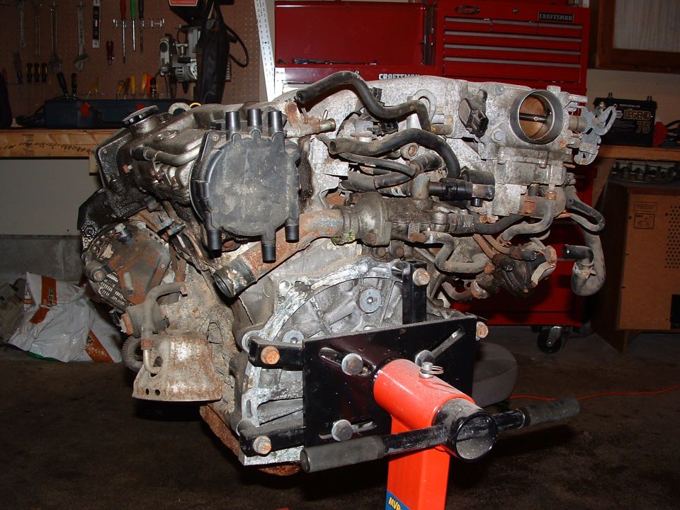 Engine on a red stand, with hoses and distributor cap visible