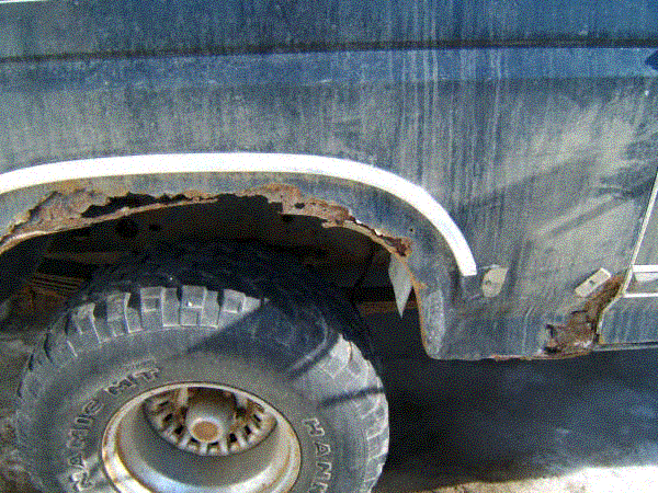 Rusted-out rear wheel arch on a blue 1980 Ford Bronco with mud-terrain tire visible