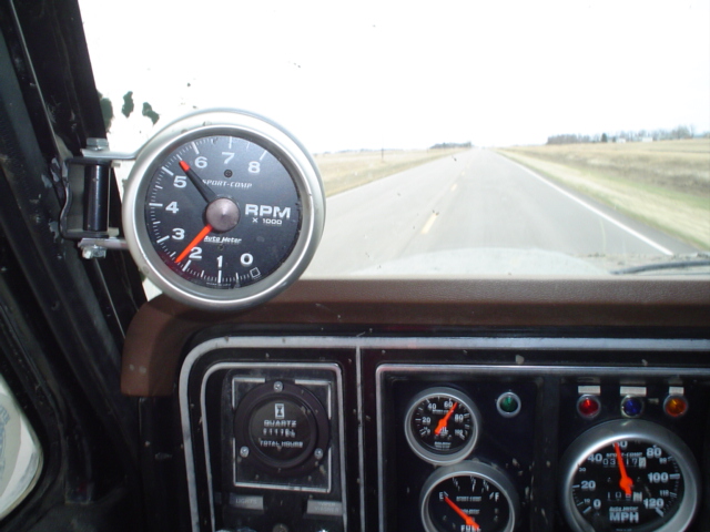 Pillar-mounted Auto Meter Sport-Comp tachometer in a truck cab, gauges and road visible below