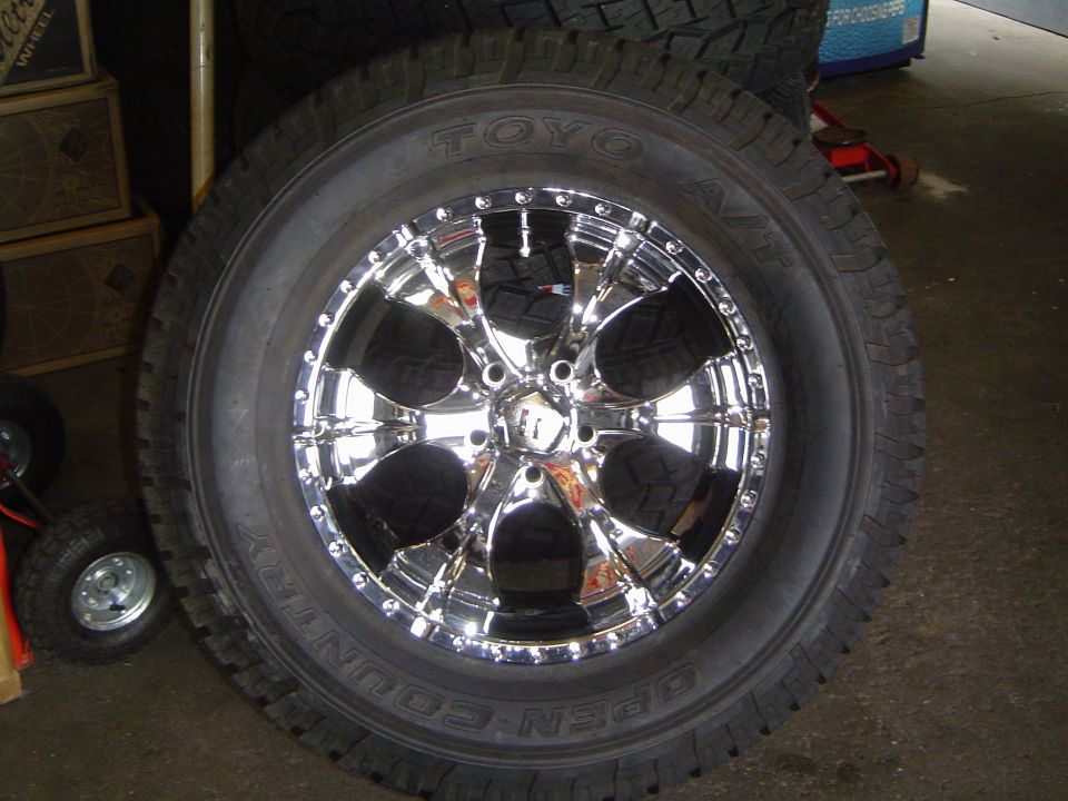 Chrome wheel on Toyo Open Country A/T tire standing in a garage